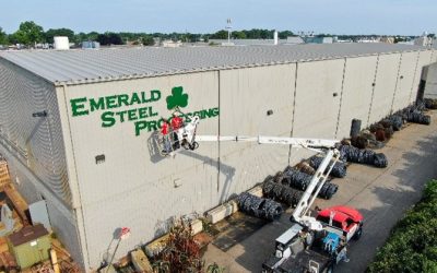 Two men in a cherry picker installing a building sign for Emerald Steel