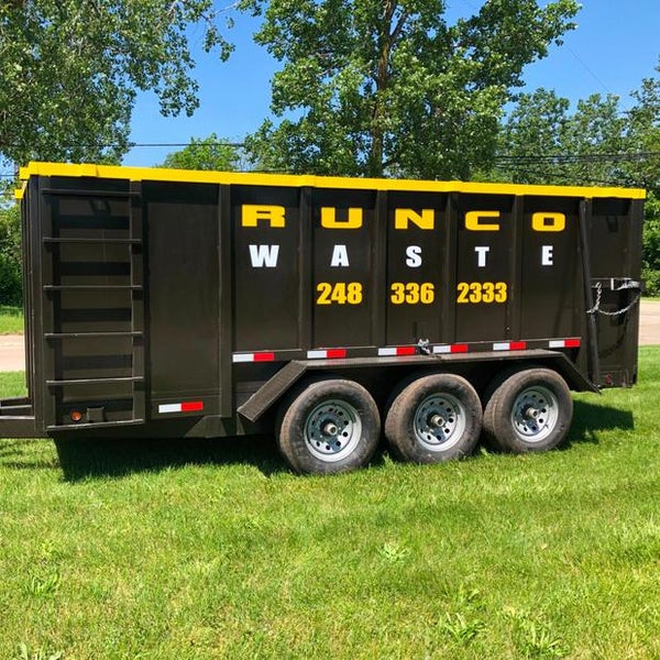 Black dumpster on wheels with yellow lettering parked on grass