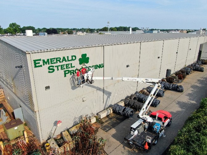 Two men in a cherry picker installing a building sign for Emerald Steel